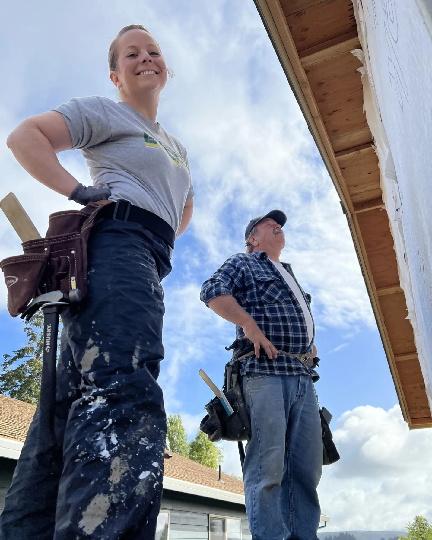 Vernonia-September-2024-website Two volunteers stand proudly at the work they are doing on home #13 in Vernonia, Oregon in September 2024.